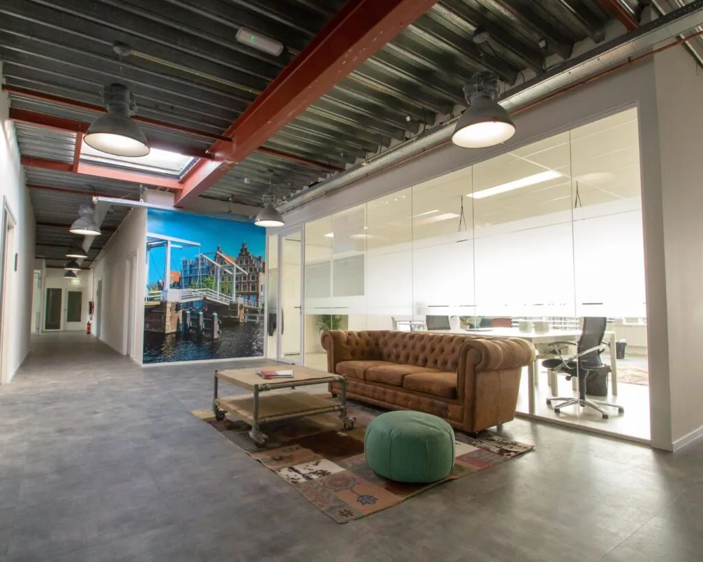 Modern ingerichte kantoorruimte aan de Bingerweg 18 met glazen vergaderruimte, industriële details en een loungehoek met leren bank.