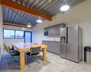 Moderne kantoorkeuken met houten vergadertafel, acht stoelen, grijze kasten en een grote RVS koelkast aan de Bingerweg 18.