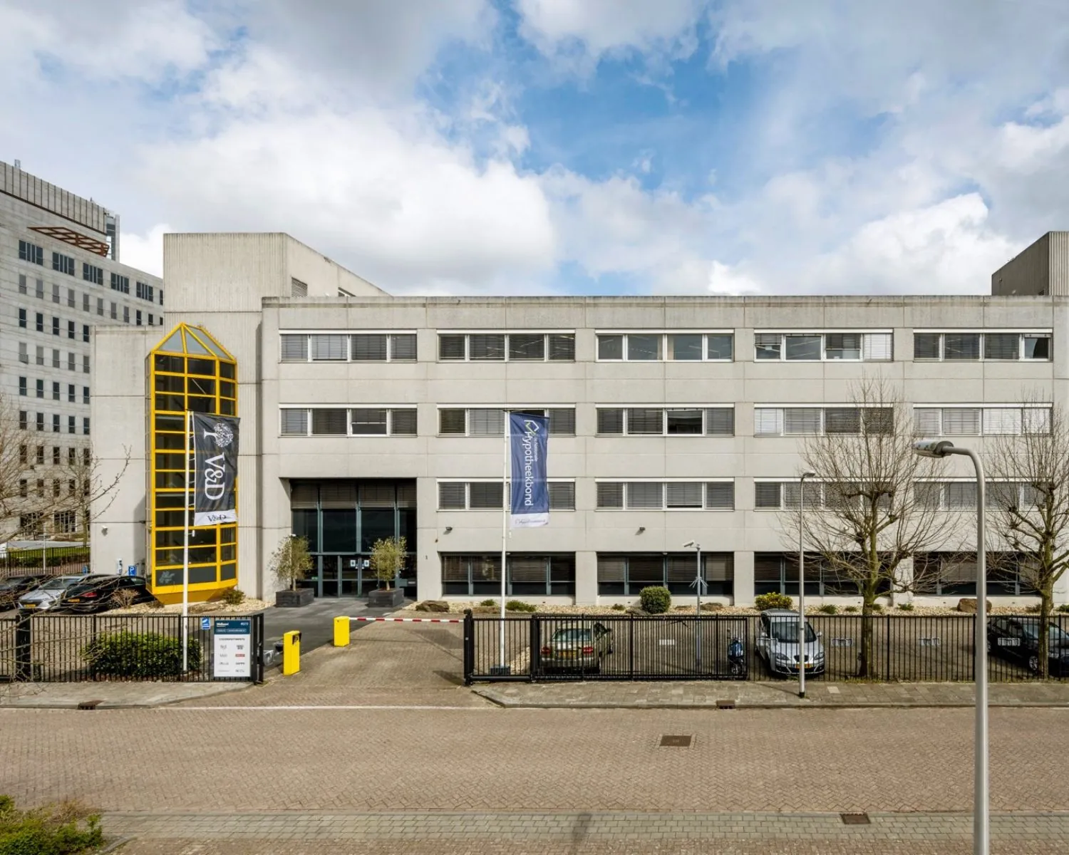 Vooraanzicht van een modern kantoorgebouw aan de Diemermere 1 in Diemen, met parkeerplaatsen en opvallende gele entree.