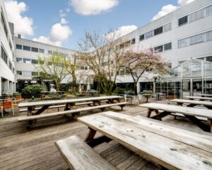 Binnenplaats van kantoorruimte aan Diemermere 1 in Diemen met houten picknicktafels, bomen en een glazen serre.