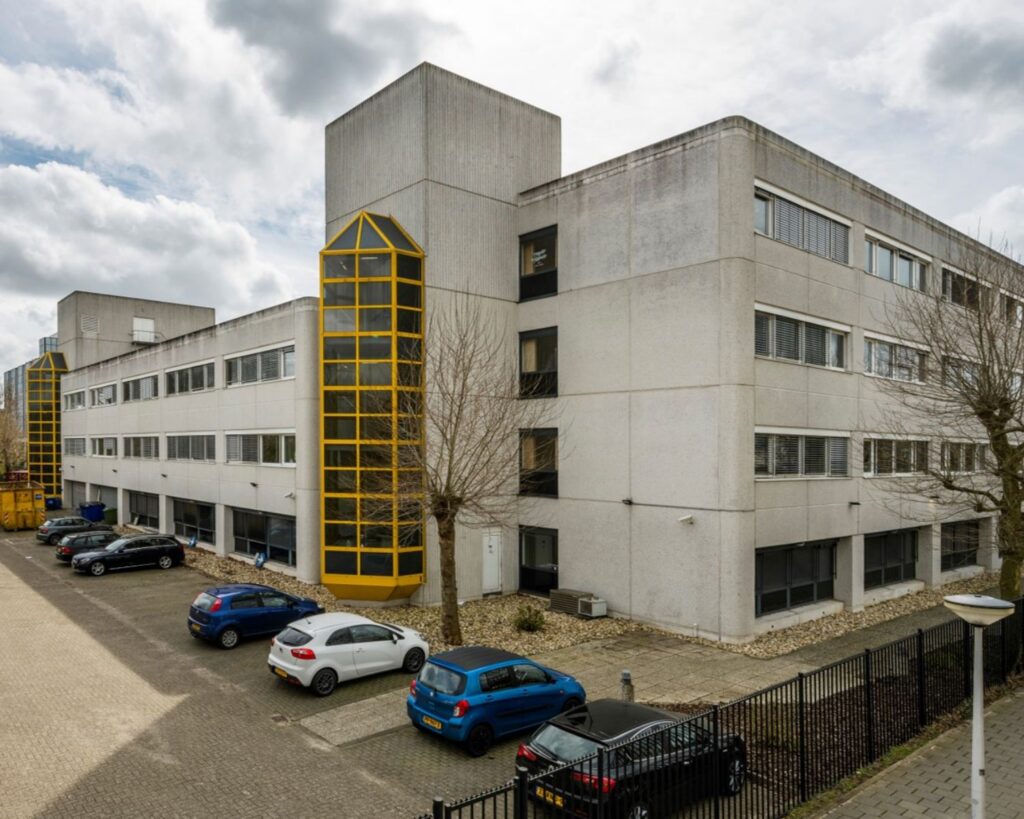 Grijs kantoorgebouw aan de Diemermere 1 in Diemen met gele accenten en een parkeerplaats ervoor.