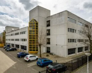 Grijs kantoorgebouw aan de Diemermere 1 in Diemen met gele accenten en een parkeerplaats ervoor.