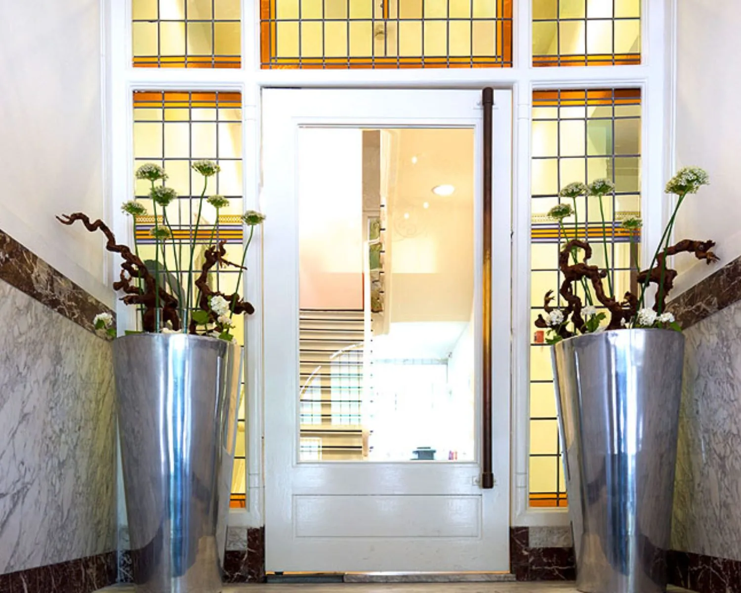Entree van een kantoorruimte aan de Emmalaan 25 in Amsterdam met marmeren muren, glas-in-loodramen en moderne plantenbakken.