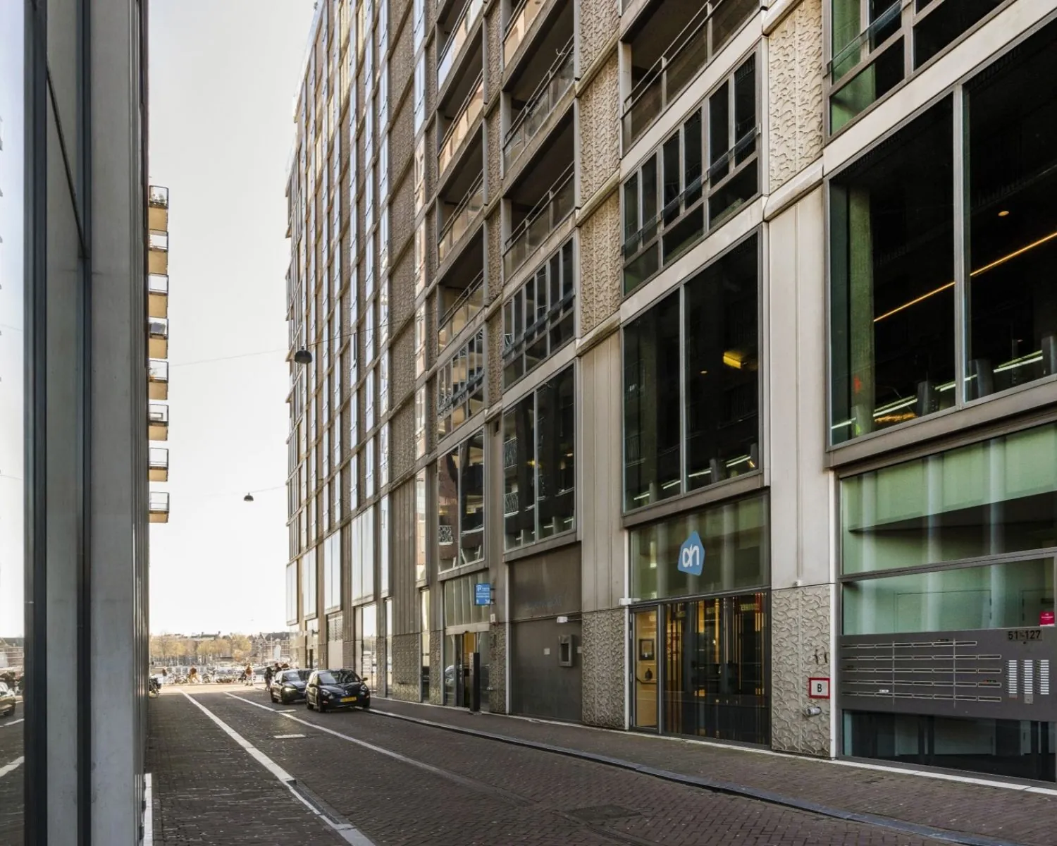 Straatbeeld van de Harry Banninkstraat in Amsterdam met een modern kantoorgebouw en een Albert Heijn-filiaal op nummer 51.