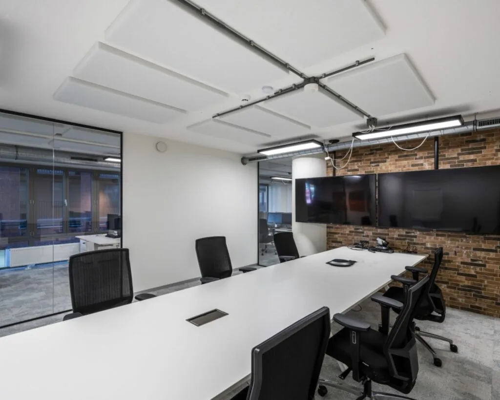 Moderne vergaderruimte met lange witte tafel, zwarte bureaustoelen en grote beeldschermen aan een bakstenen muur aan de Harry Banninkstraat 51 in Amsterdam.