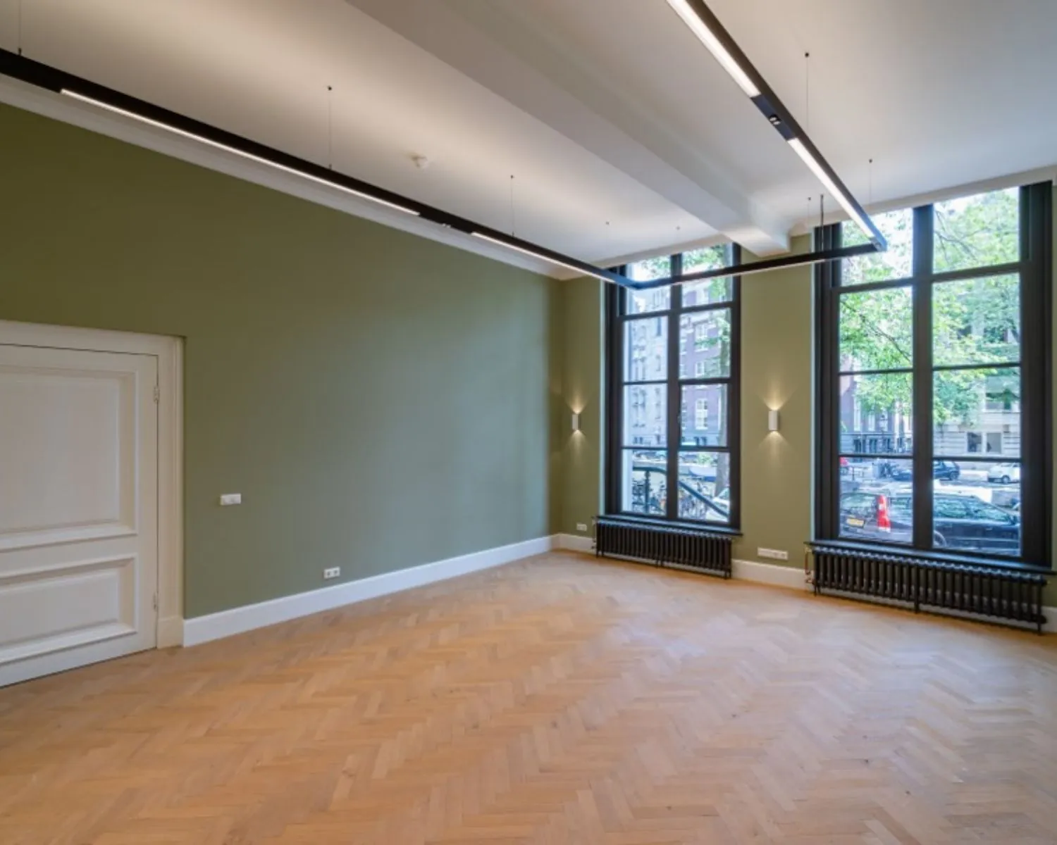 Lichte kantoorruimte aan de Herengracht 174 in Amsterdam met grote ramen, visgraat houten vloer en groene muur.