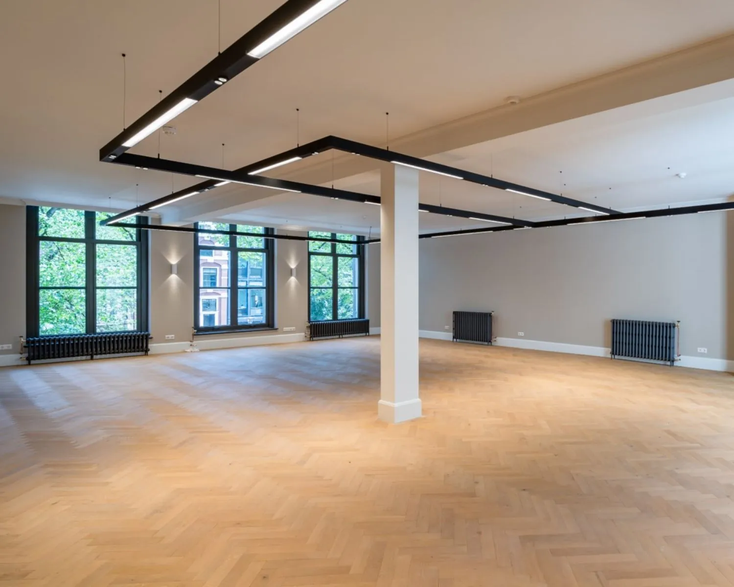 Ruime, moderne kantoorruimte met grote ramen en houten visgraatvloer aan de Herengracht 174 in Amsterdam.