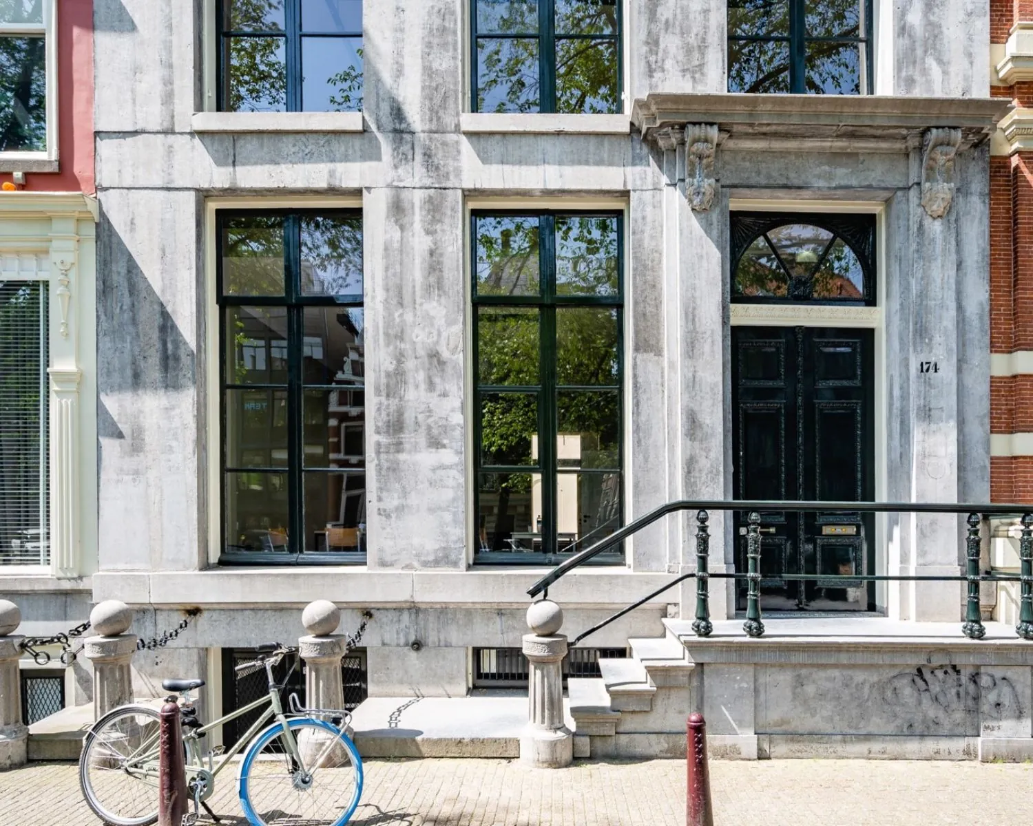 Voorgevel van een monumentaal grachtenpand aan de Herengracht 174 in Amsterdam met grote ramen, een zwarte voordeur en een fiets ervoor.