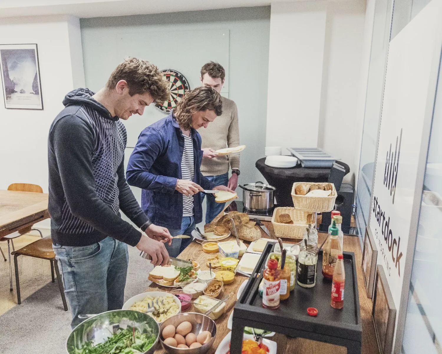 Drie mannen bereiden lunch bij een buffet met brood en beleg in een gemeenschappelijke ruimte van een kantoor aan de Herengracht 420 in Amsterdam.