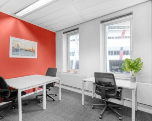 Moderne kantoorruimte met drie bureaus, rode accentmuur en uitzicht op de Johan Cruijff Boulevard.
