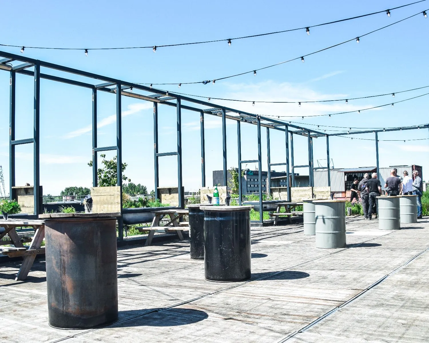 Dakterras met picknicktafels, olievaten als statafels en uitzicht op de omgeving bij Johan Huizingalaan 763A in Amsterdam.