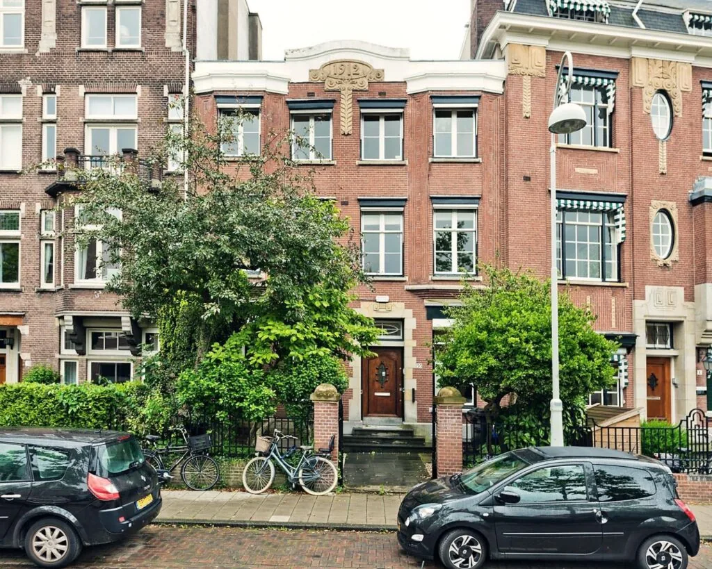 Voorgevel van een klassiek kantoorpand aan de Johannes Vermeerstraat 55 in Amsterdam met bakstenen gevel, bomen en geparkeerde auto's.