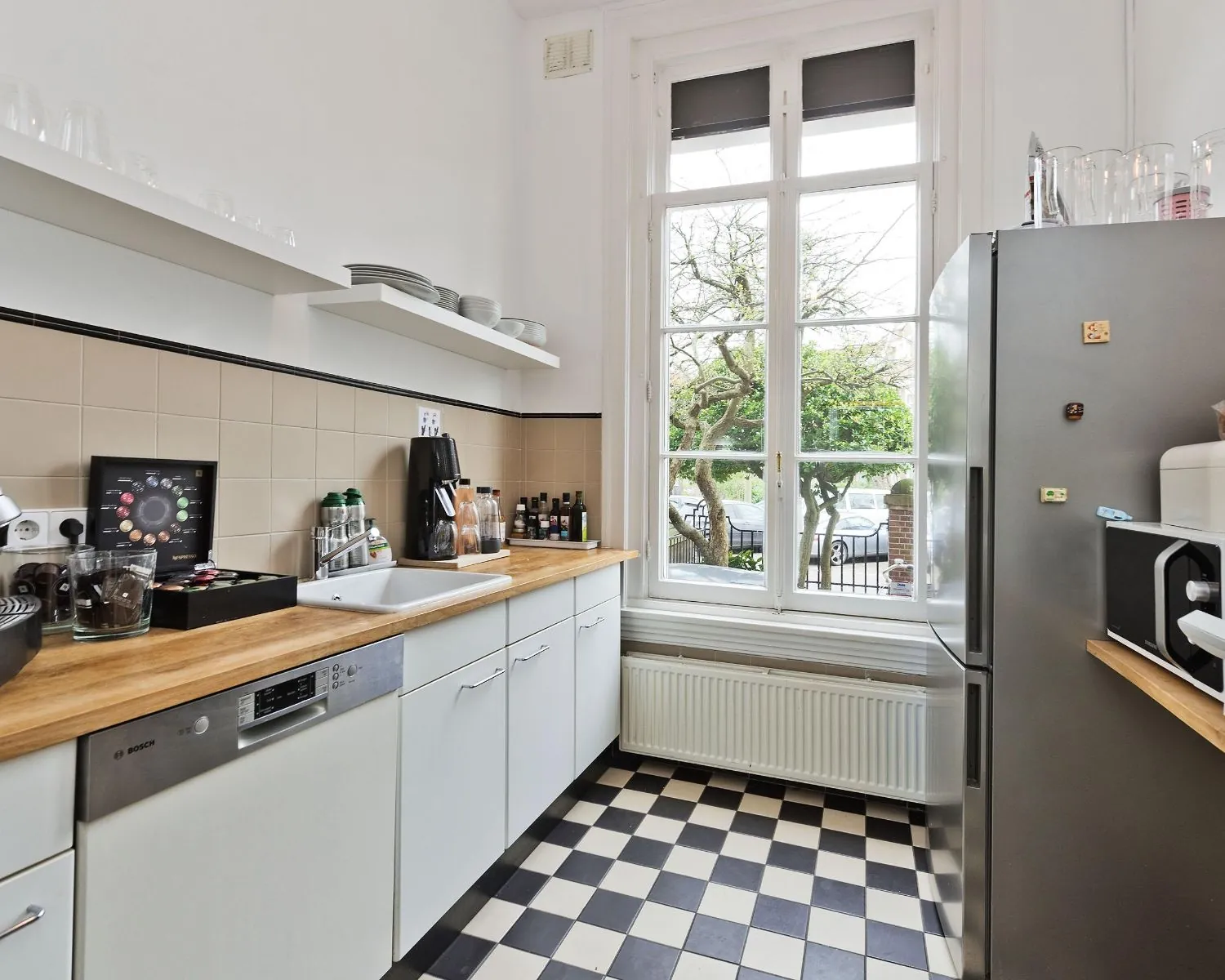 Moderne pantry in een kantoorruimte aan de Johannes Vermeerstraat 55 in Amsterdam met zwart-wit geblokte vloer en groot raam met uitzicht op de straat.