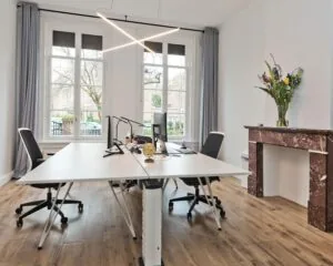 Moderne kantoorruimte aan de Johannes Vermeerstraat 55 in Amsterdam met grote ramen, strakke bureaus en een marmeren schouw.