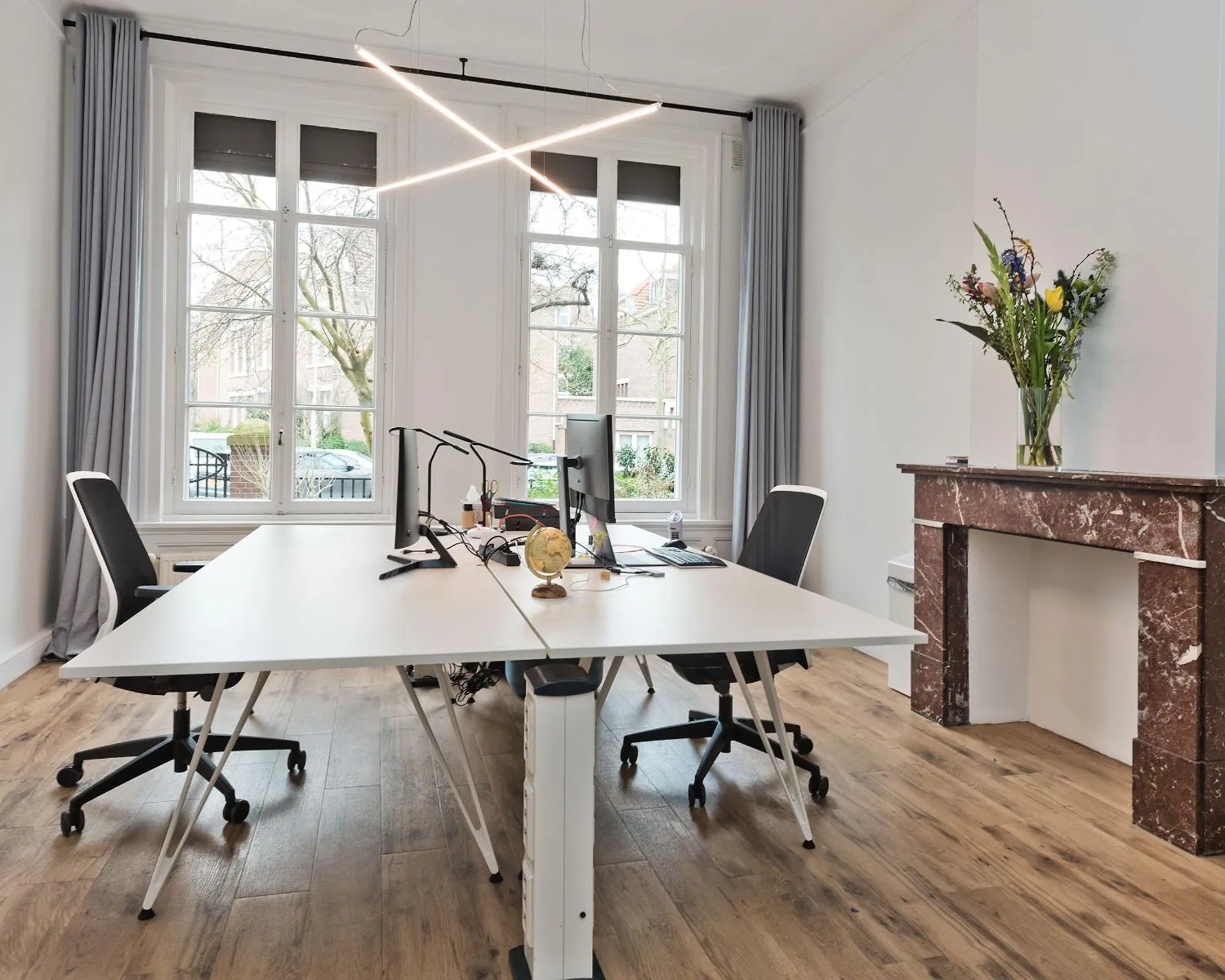 Moderne kantoorruimte aan de Johannes Vermeerstraat 55 in Amsterdam met grote ramen, strakke bureaus en een marmeren schouw.