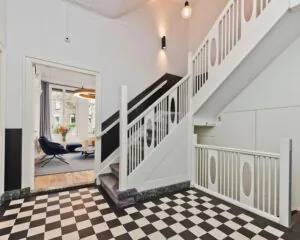 Entreehal met zwart-wit geblokte vloer, witte trap en zicht op een moderne kantoorruimte aan de Johannes Vermeerstraat 55 in Amsterdam.