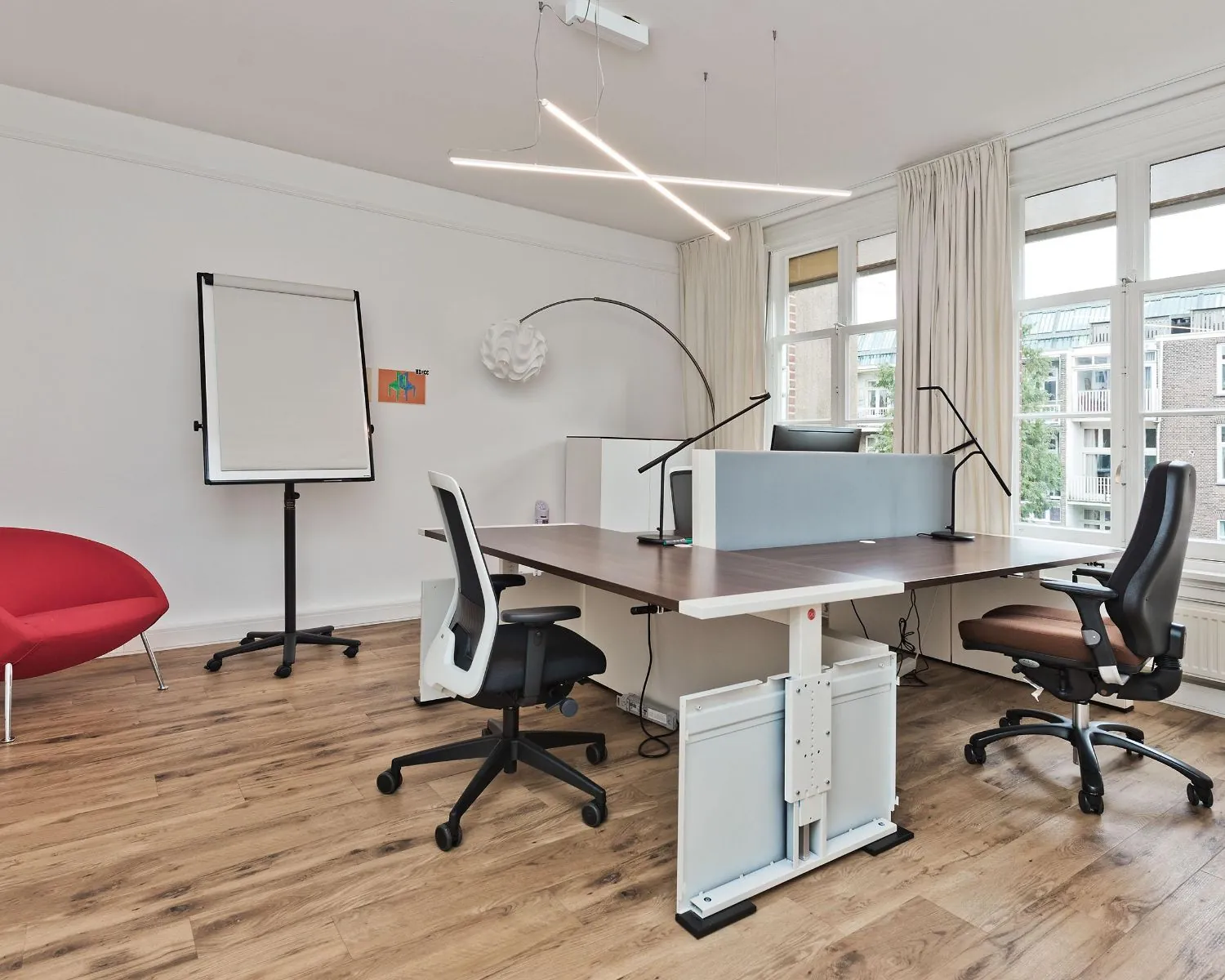 Moderne, lichte kantoorruimte aan de Johannes Vermeerstraat 55 in Amsterdam met bureaus, bureaustoelen en grote ramen.