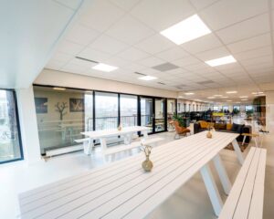Moderne kantoorruimte aan de Joop Geesinkweg 140-199 in Amsterdam met witte picknicktafels, glazen wanden en een loungehoek.