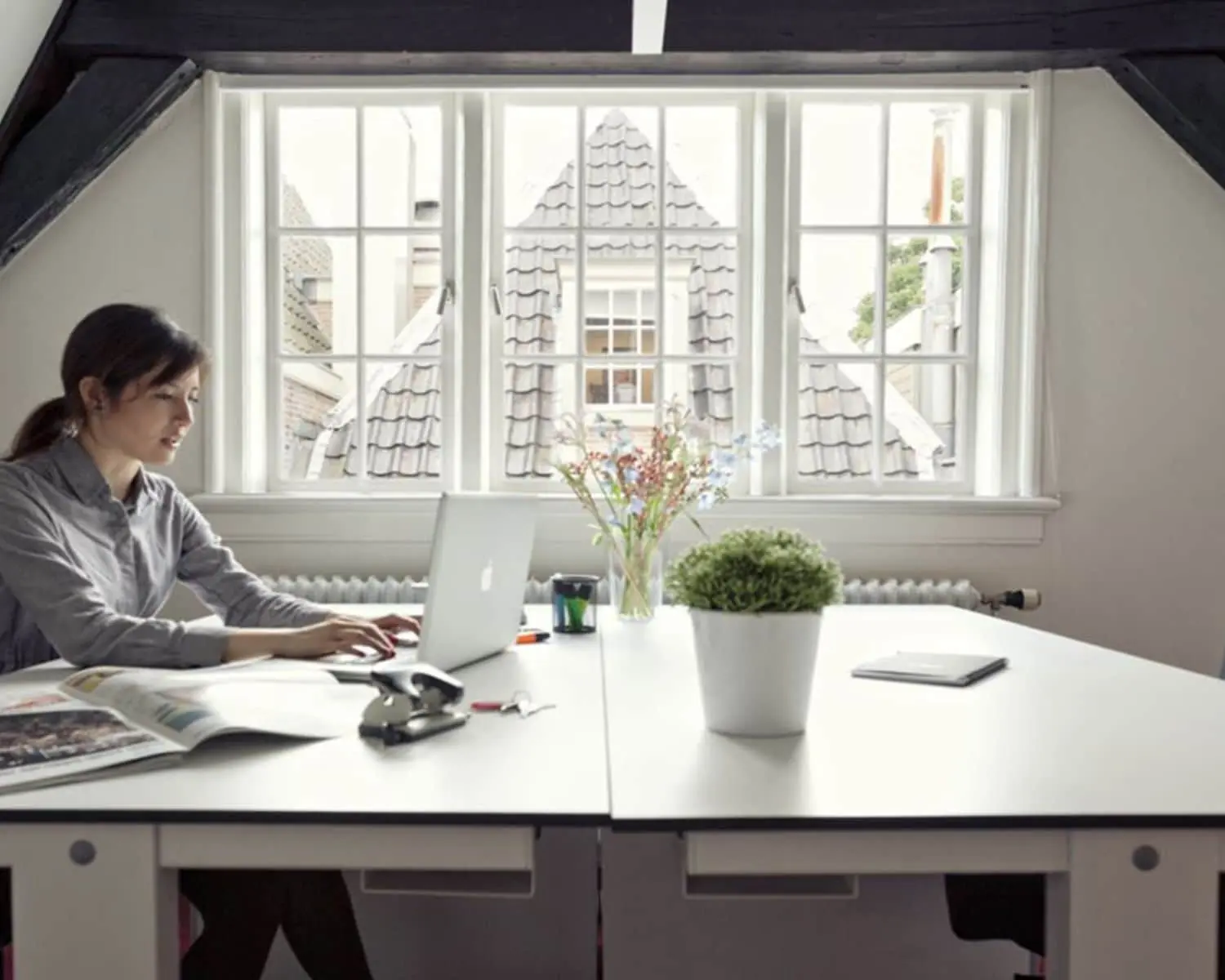 Vrouw werkt op een laptop in een lichte kantoorruimte aan de Keizersgracht met uitzicht op Amsterdamse daken.