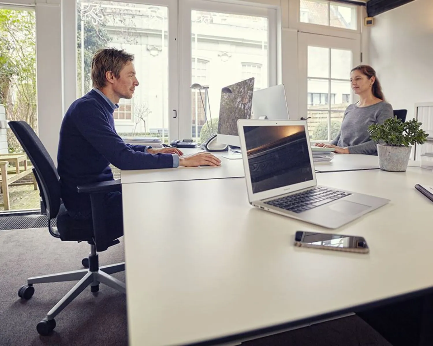 Twee mensen werken tegenover elkaar in een moderne kantoorruimte aan de Keizersgracht 106 in Amsterdam.