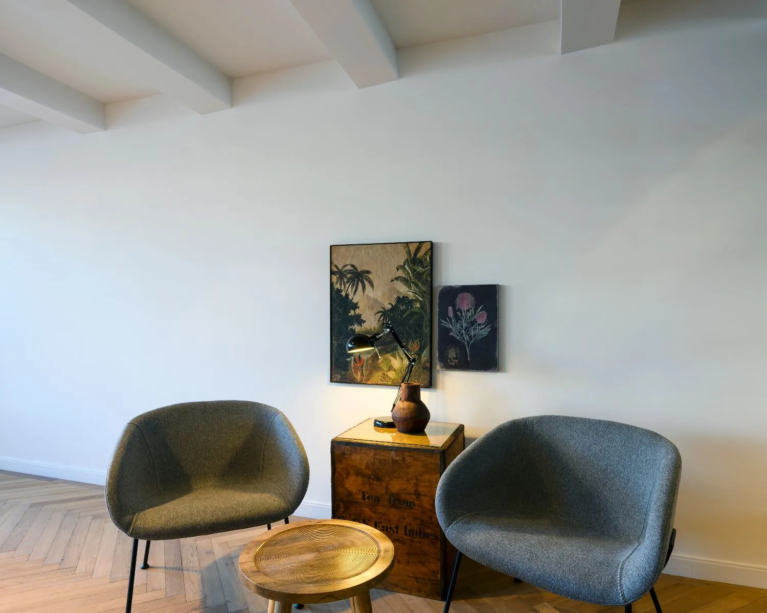 Moderne zithoek in een kantoor aan de Keizersgracht 121 in Amsterdam met twee grijze stoelen, een houten bijzettafeltje en kunst aan de muur.