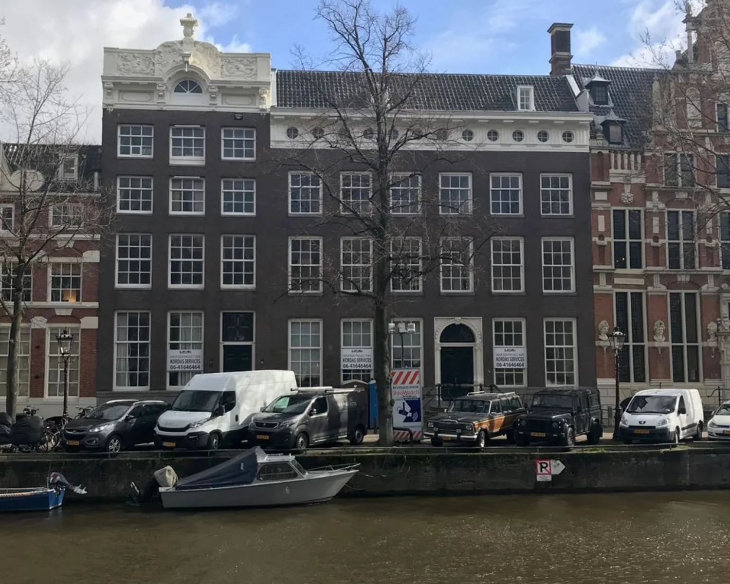 Gevel van het kantoorpand aan de Keizersgracht 121 in Amsterdam met geparkeerde auto's en boten aan de gracht.