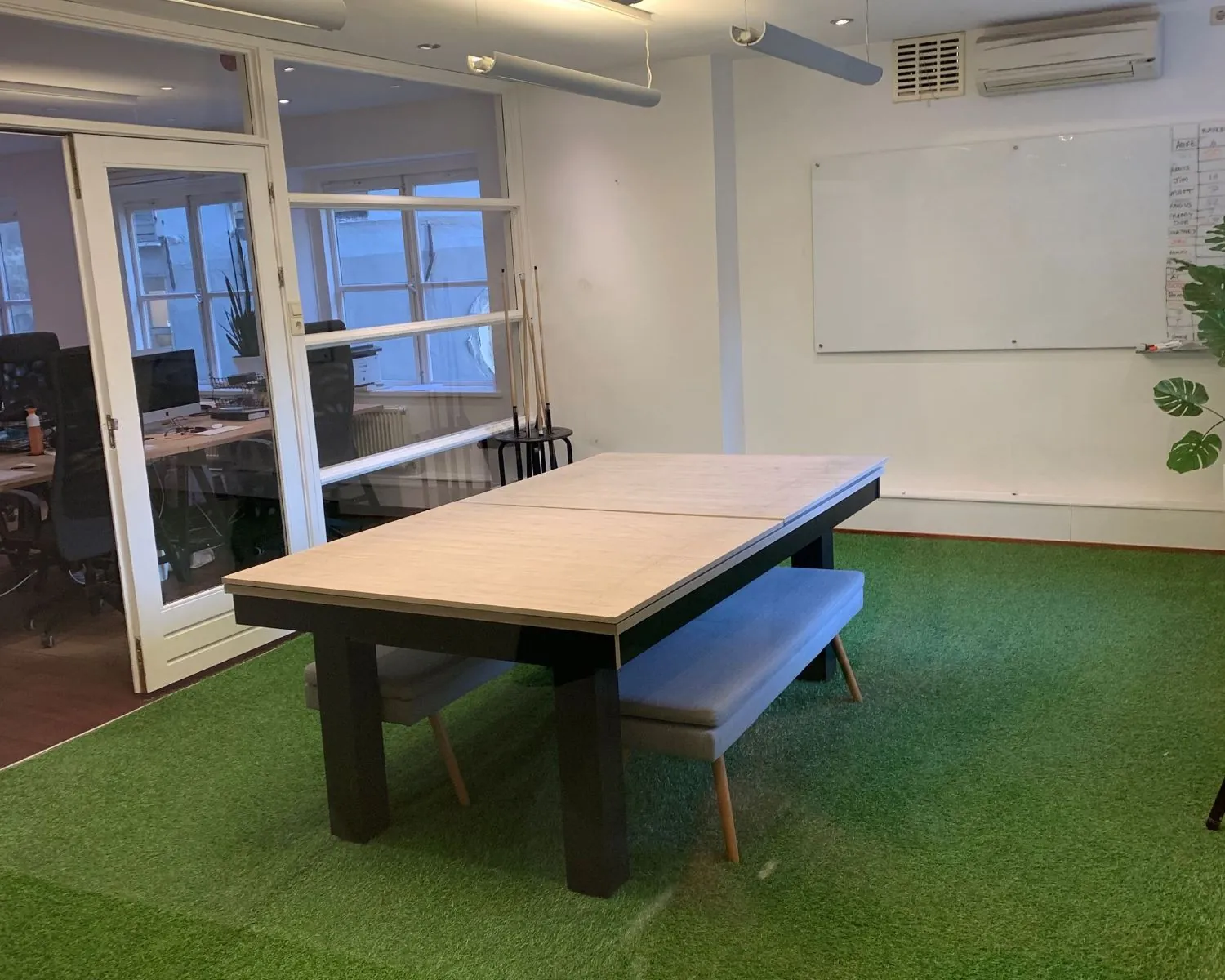 Moderne vergaderruimte aan de Keizersgracht 205 in Amsterdam met een houten tafel, kunstgrasvloer en glazen wand naar het kantoor.