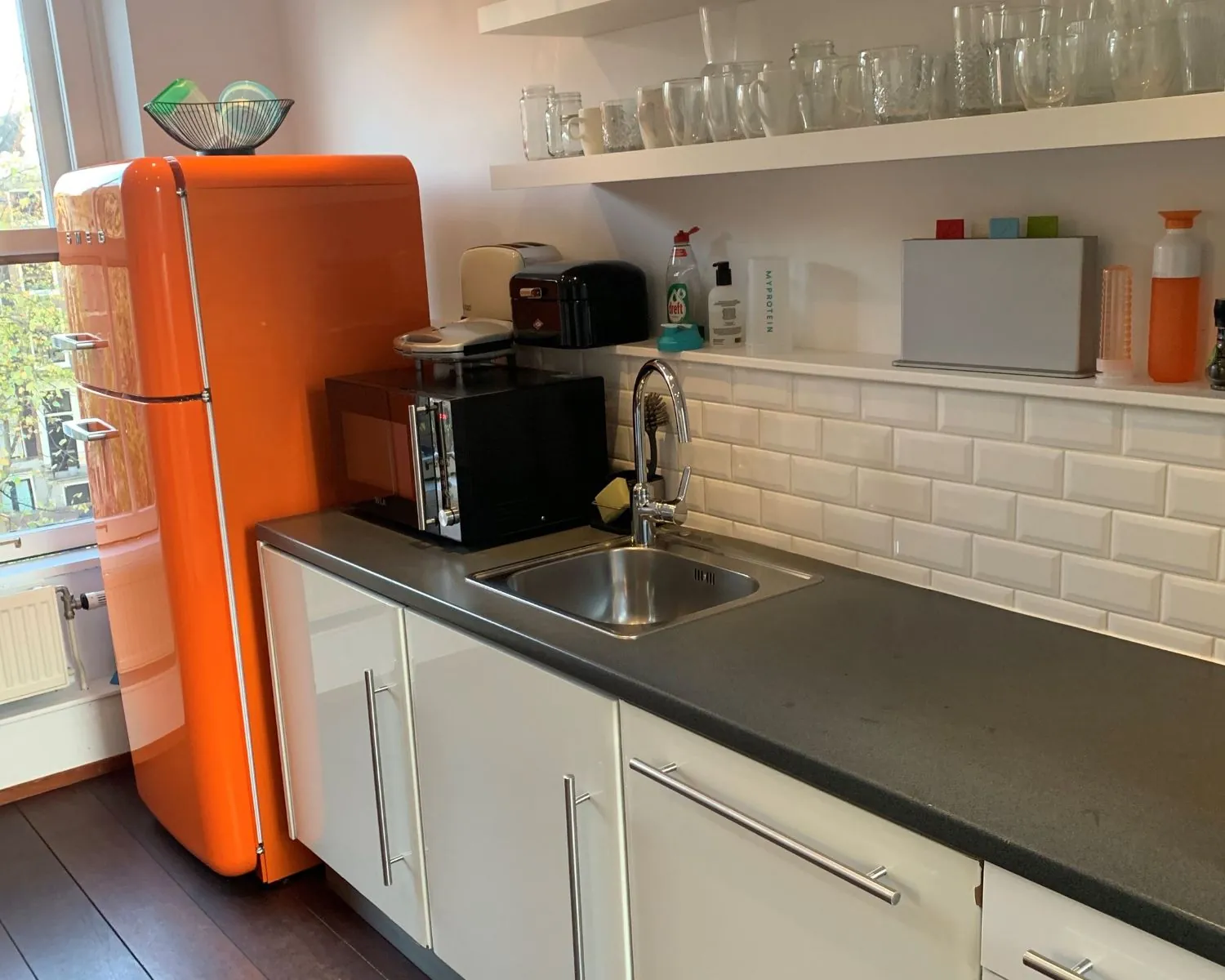 Moderne kantoorkeuken aan de Keizersgracht 205 in Amsterdam met oranje retro koelkast en witte kasten.
