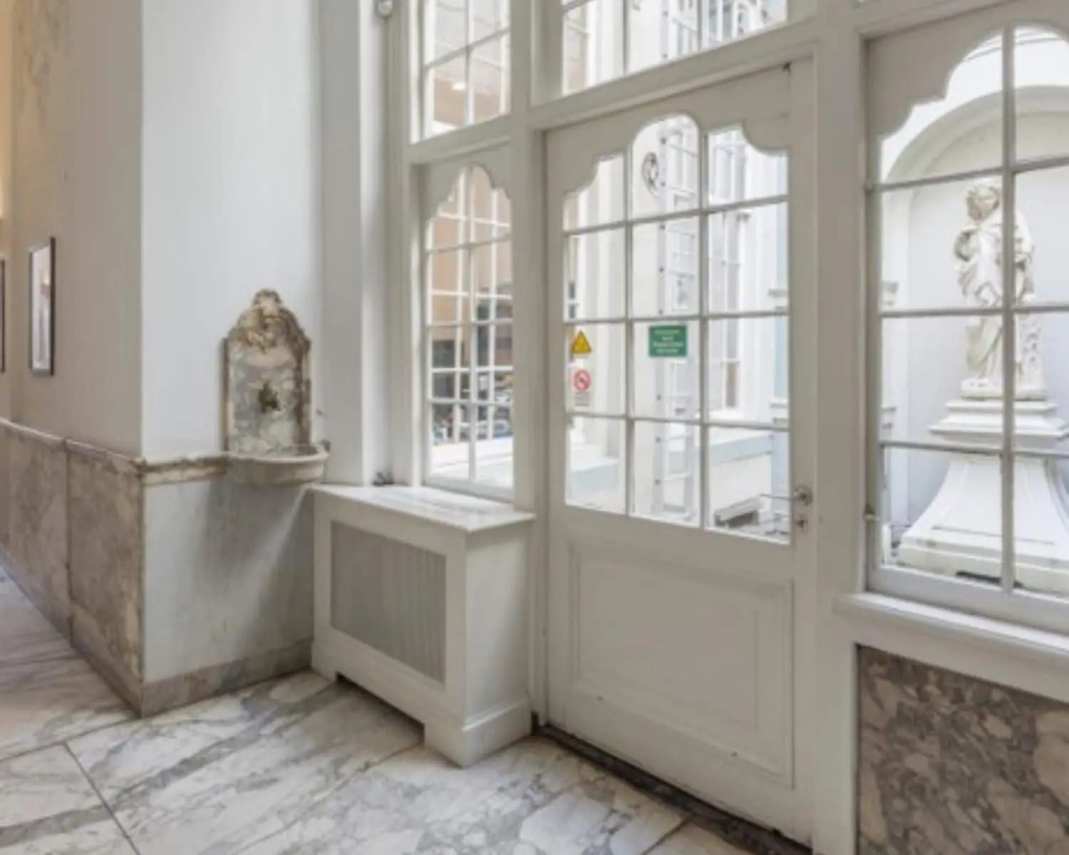 Lichte marmeren gang met klassieke details en uitzicht op een binnentuin met een standbeeld, in kantoorruimte aan de Keizersgracht 321 in Amsterdam.
