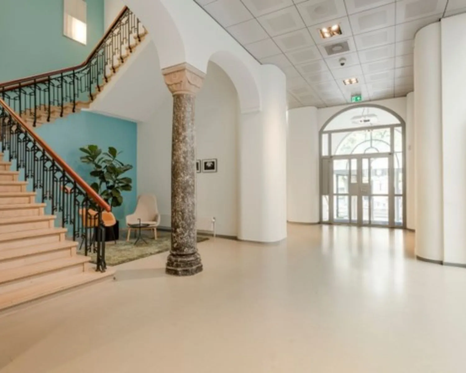 Moderne, lichte entreehal van een kantoorpand aan de Keizersgracht 617 in Amsterdam met een trap, zitgedeelte en glazen toegangsdeur.