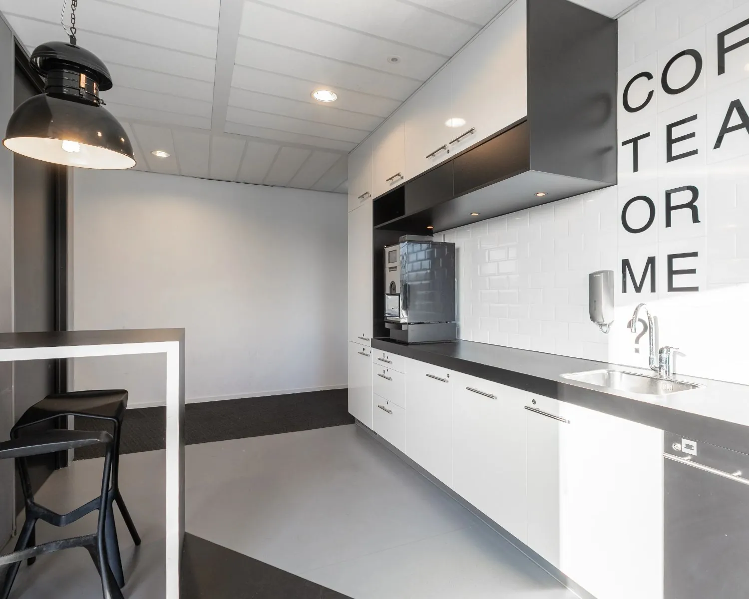 Moderne kantoorkeuken aan de Kingsfortweg 151 in Amsterdam met witte kasten, zwarte accenten en de tekst "COFFEE, TEA OR ME" op de tegelwand.
