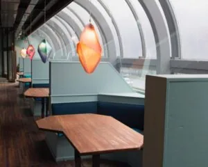 Moderne kantoorruimte aan de Maasboulevard 100 in Rotterdam met houten zithoeken en kleurrijke hanglampen langs een gebogen glazen wand.