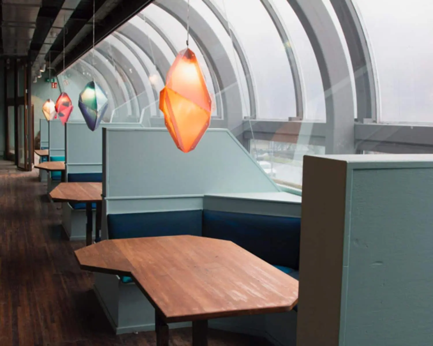 Moderne kantoorruimte aan de Maasboulevard 100 in Rotterdam met houten zithoeken en kleurrijke hanglampen langs een gebogen glazen wand.