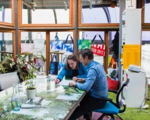 Een moderne kantoorruimte aan de Maasboulevard 100 in Rotterdam met twee mensen werkend aan een kleurrijke tafel, omgeven door planten en designitems.