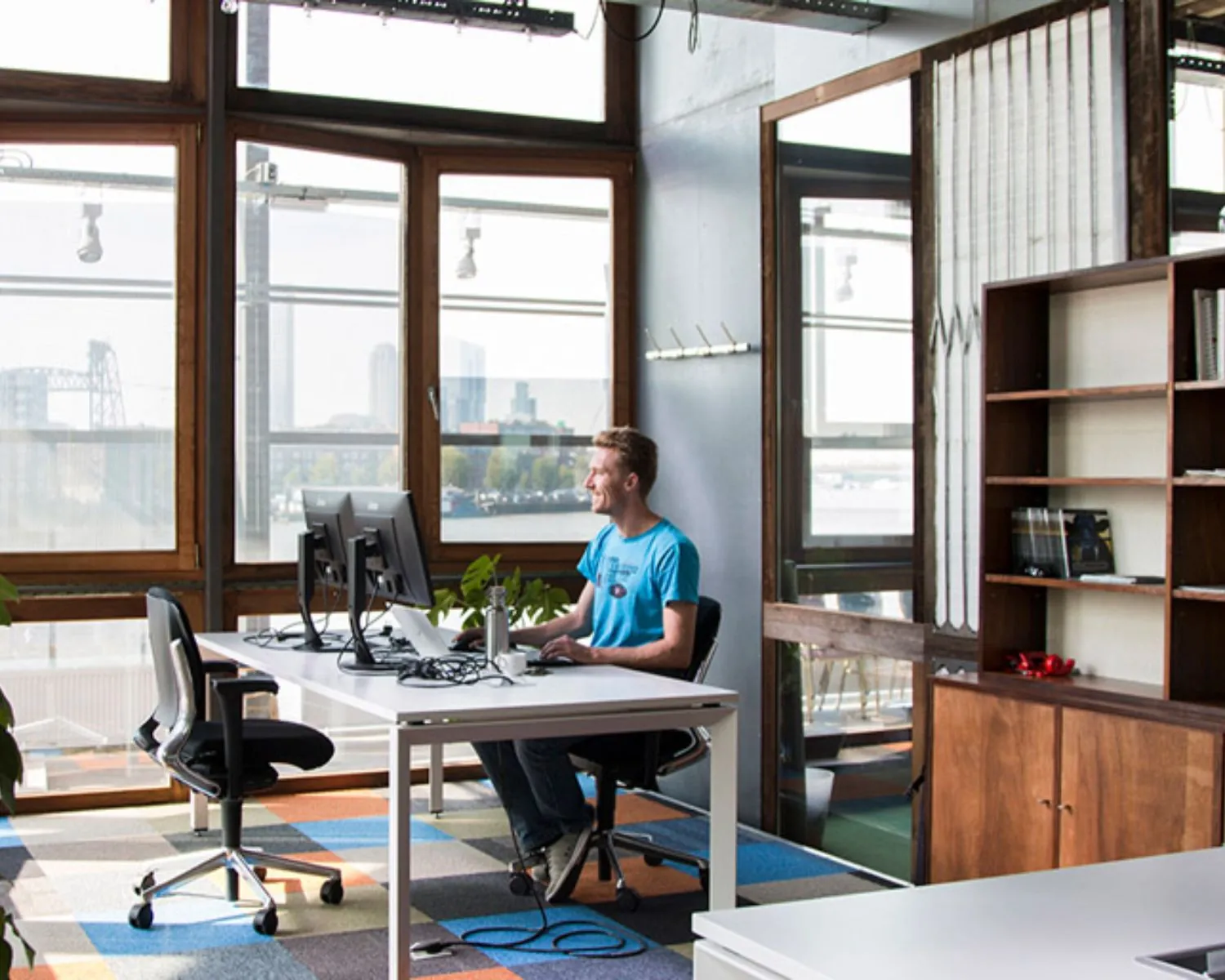 Moderne kantoorruimte aan de Maasboulevard 100 in Rotterdam met uitzicht op de stad en een werkplek met twee beeldschermen.