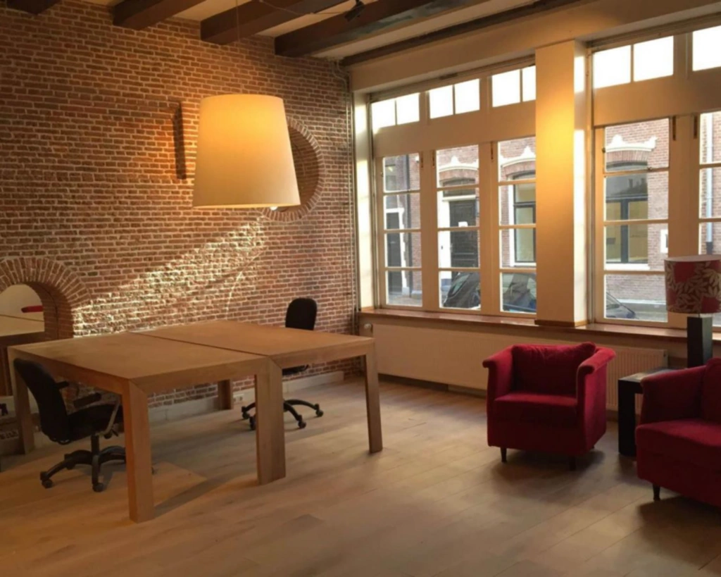 Sfeervolle kantoorruimte aan het Molenpad 3 in Amsterdam met bakstenen muur, houten meubels en grote ramen.