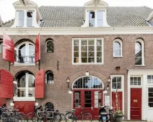 Voorgevel van een karakteristiek kantoorpand aan het Molenpad 3 in Amsterdam met rode luiken en geparkeerde fietsen.