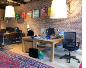 Moderne kantoorruimte aan het Molenpad 3 in Amsterdam met bakstenen muren, houten bureaus en kleurrijke wandposters.
