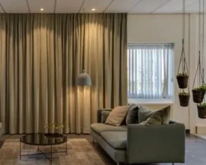 Moderne en sfeervol ingerichte kantoorruimte aan de Mr. E.N. van Kleffenstraat 6 in Arnhem met comfortabele zithoek, hangplanten en grote gordijnen.