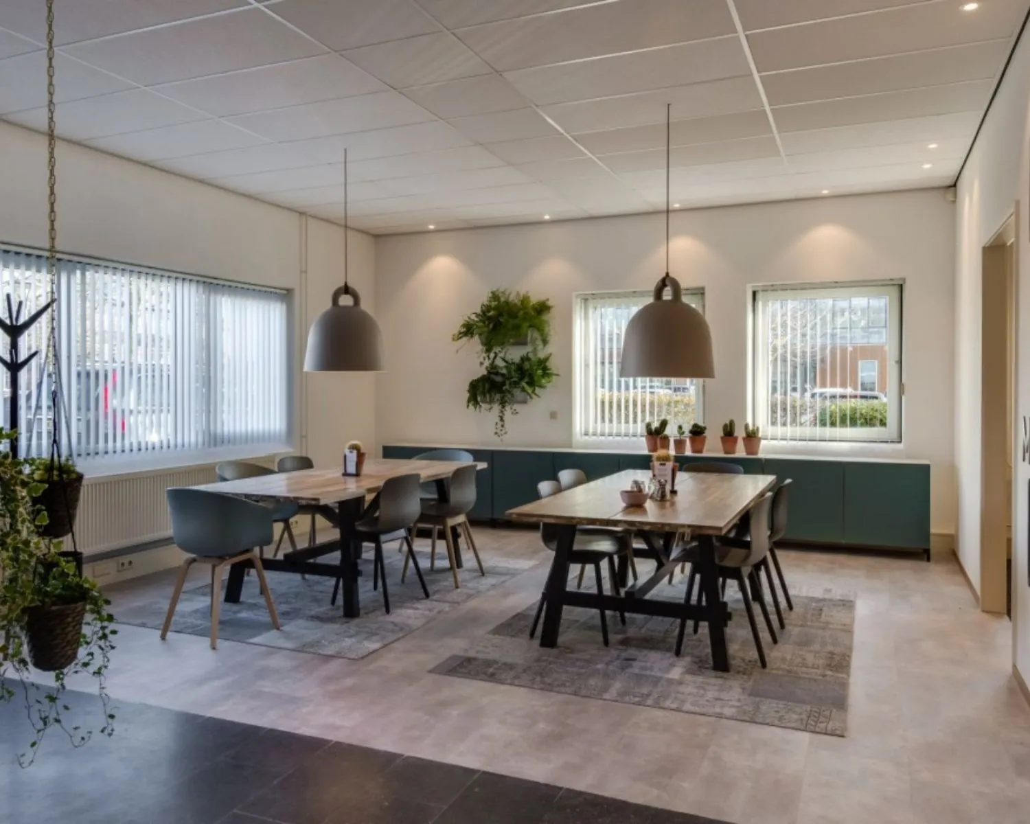 Moderne kantoorruimte aan de Mr. E.N. van Kleffenstraat 6 in Arnhem met twee houten vergadertafels, designstoelen, hanglampen en veel daglicht.
