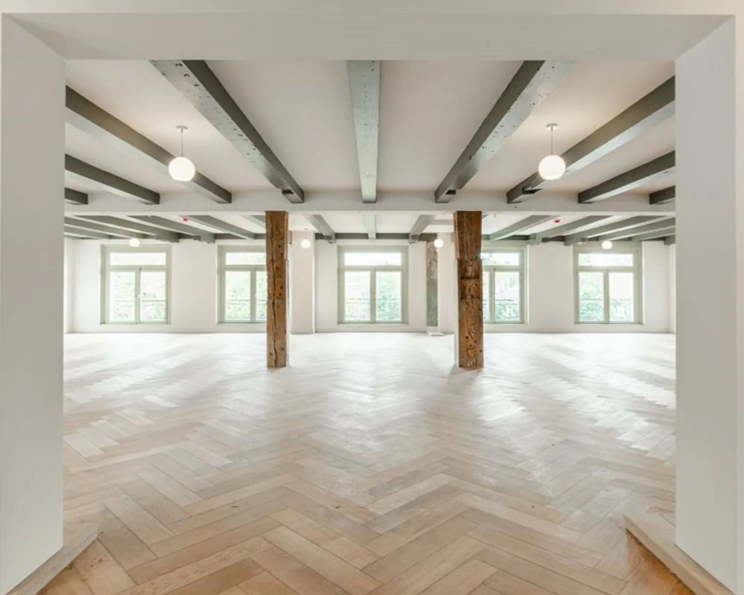 Lichte, open kantoorruimte met houten visgraatvloer en houten steunpilaren aan de Nieuwe Herengracht 95 in Amsterdam.