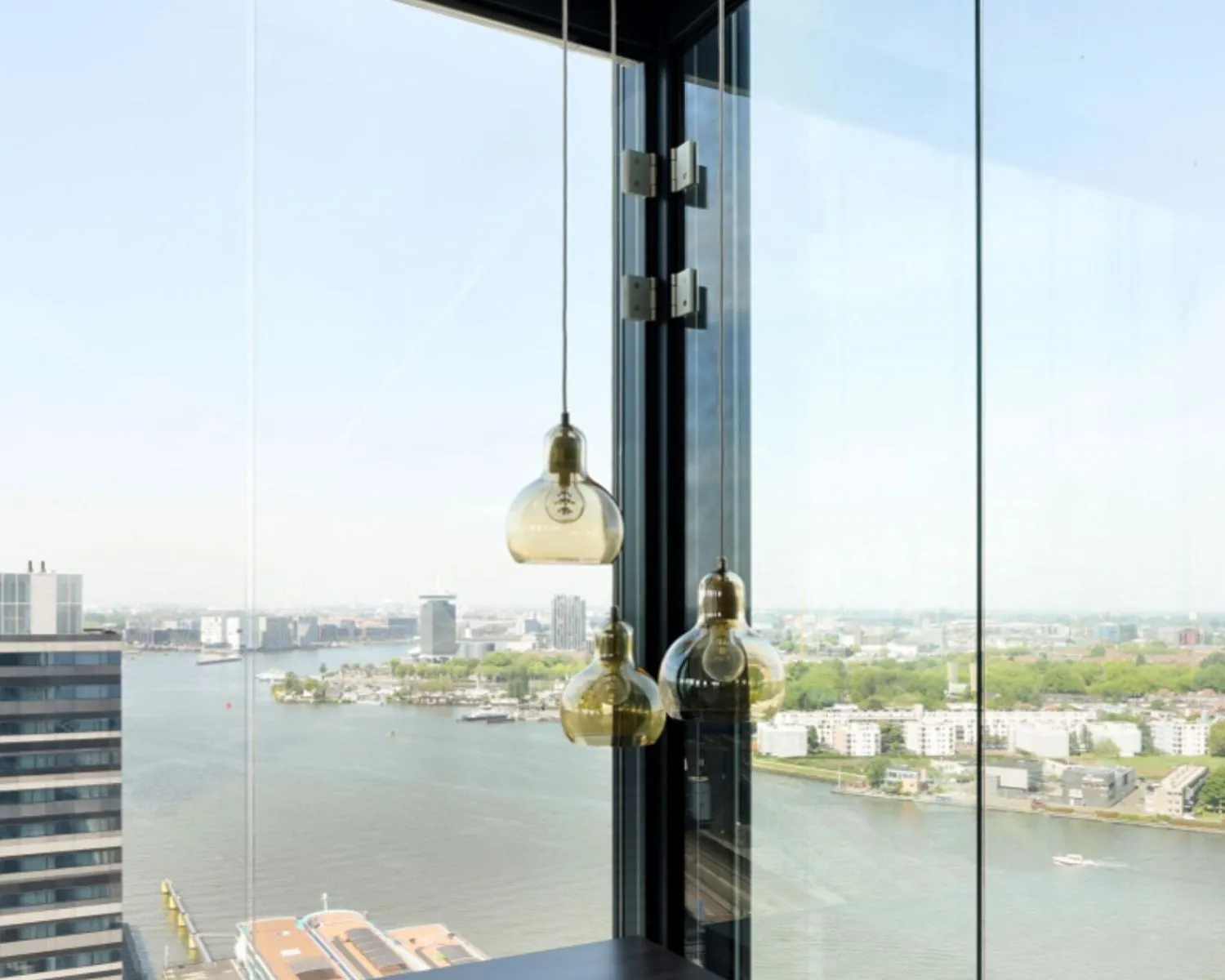 Modern kantoorinterieur met hanglampen en panoramisch uitzicht over het IJ vanaf Piet Heinkade 55 in Amsterdam.