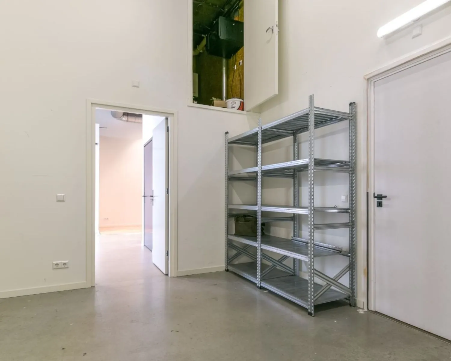 Opslagruimte in bedrijfsunit aan Poortland 242 met metalen stellingkast en open deur naar aangrenzende ruimte.