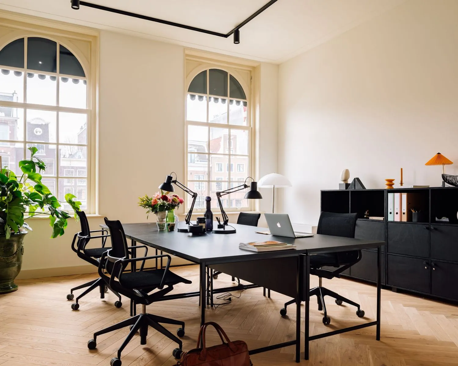 Moderne en lichte kantoorruimte aan de Prinsengracht met zwarte bureaus, bureaustoelen, grote ramen en planten.