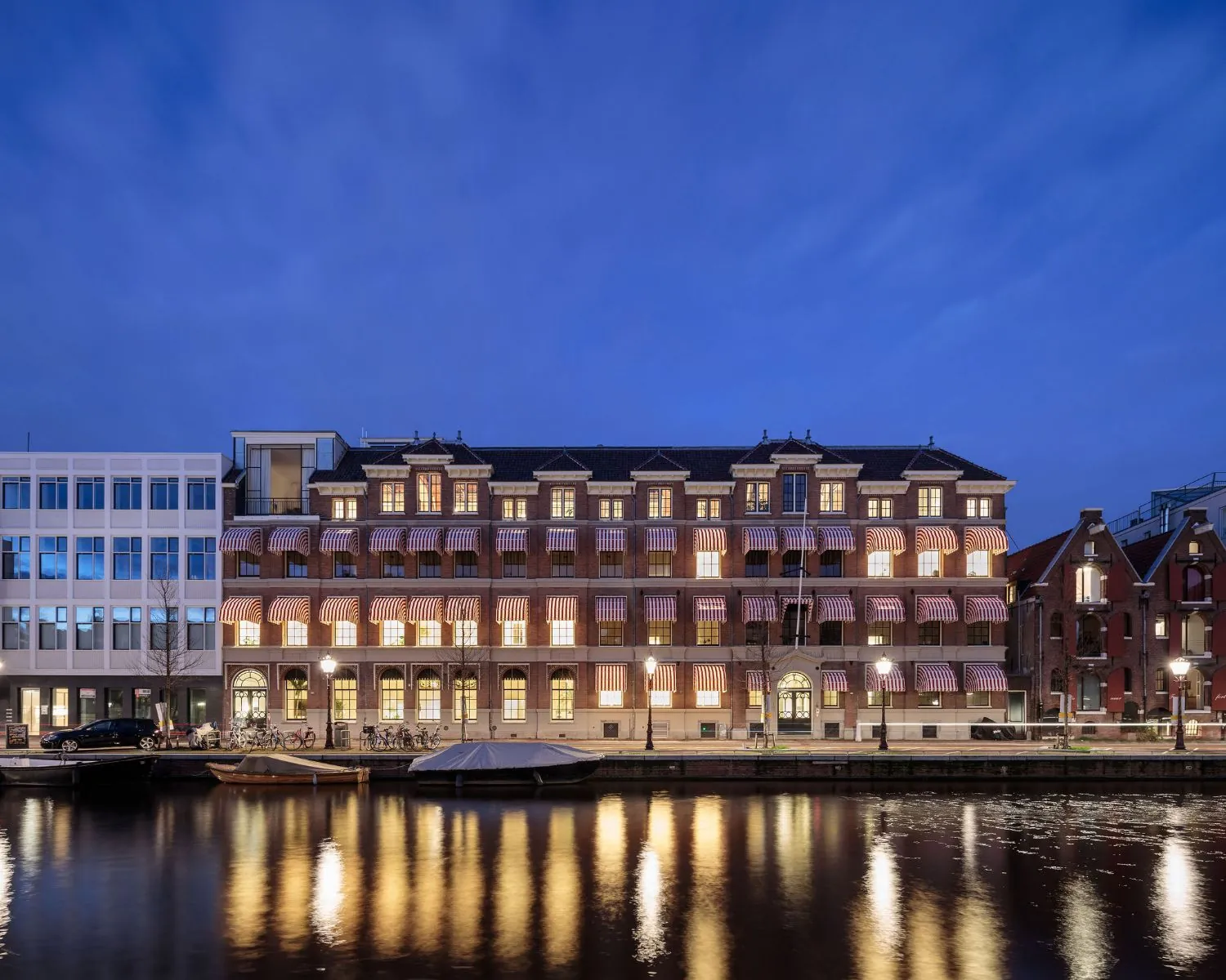Verlichte kantoorruimte aan de Prinsengracht 769 in Amsterdam, weerspiegeld in het water tijdens de avond.