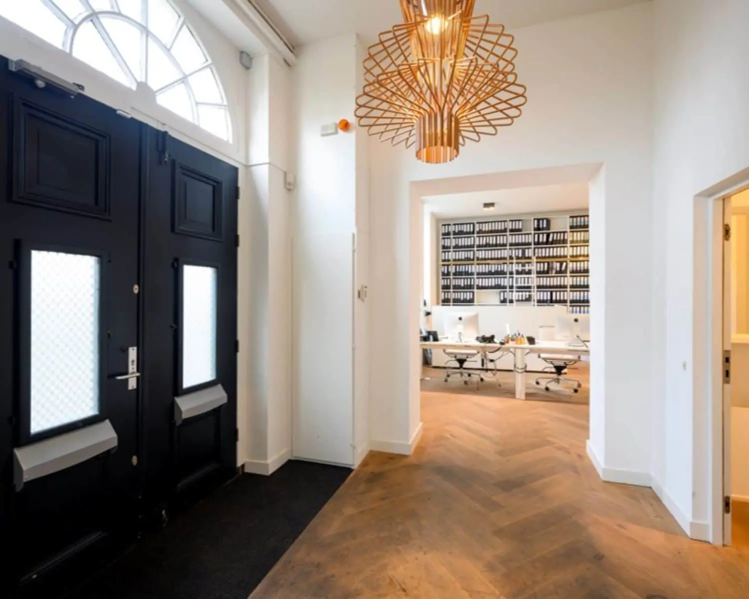 Moderne entree met houten visgraatvloer en uitzicht op een lichte kantoorruimte aan de Sarphatistraat 640-642 in Amsterdam.