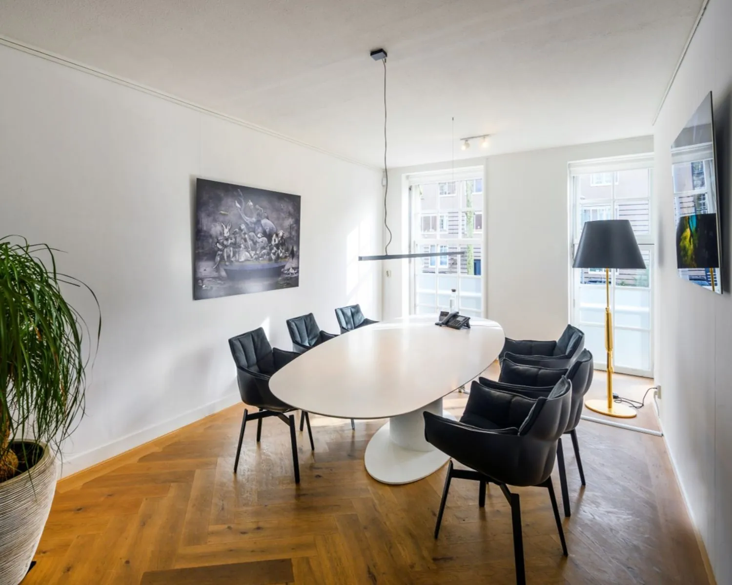 Moderne vergaderruimte met ovale tafel en zes zwarte stoelen aan de Sarphatistraat in Amsterdam.