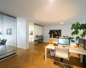 Moderne kantoorruimte aan de Sarphatistraat in Amsterdam met houten vloer, glazen wanden en een stijlvol ingericht bureau.
