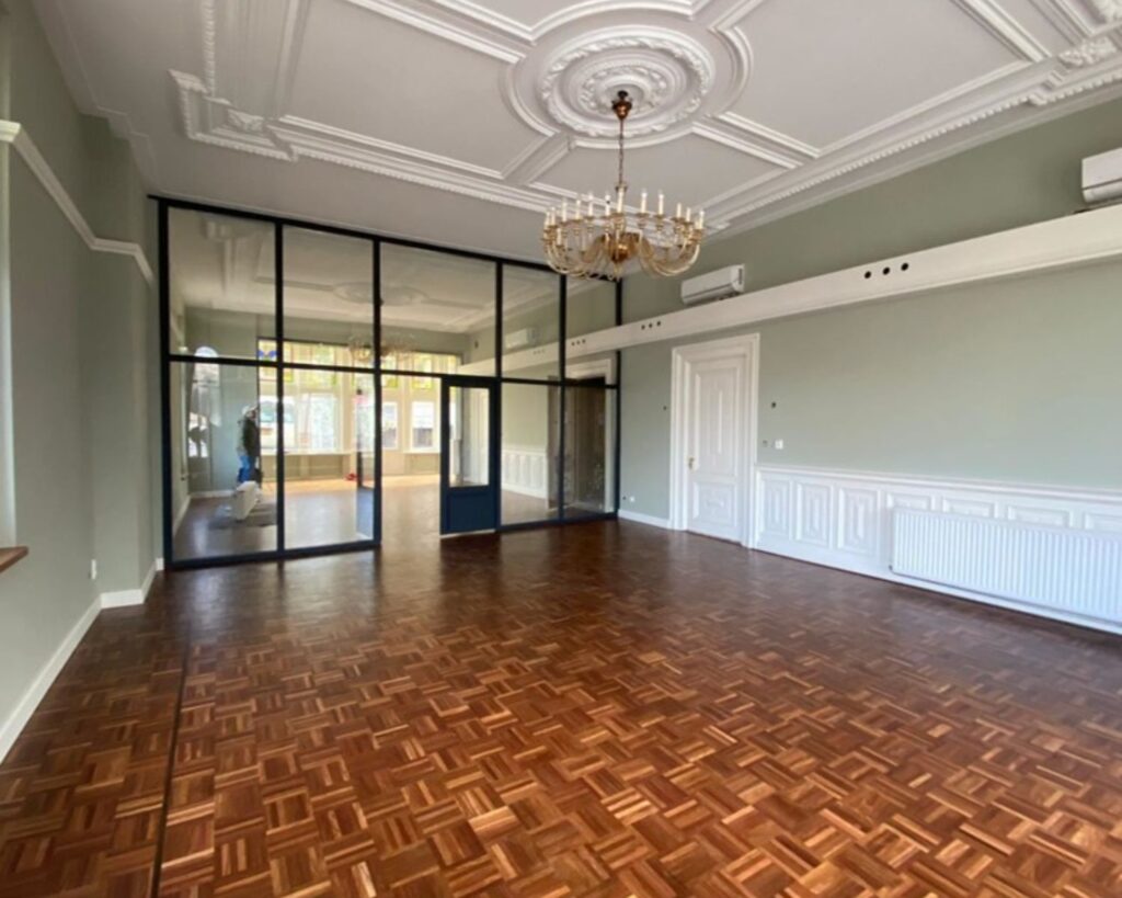 Luxe kantoorruimte aan de Stadhouderskade 160 in Amsterdam met hoog plafond, houten visgraatvloer, sierplafond en glazen scheidingswand.