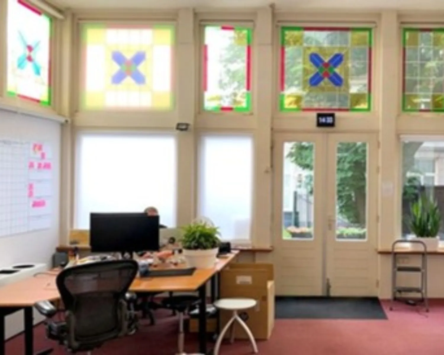 Lichte kantoorruimte aan de Stadhouderskade 160 in Amsterdam met grote ramen, glas-in-lood details en bureaus met computerschermen.